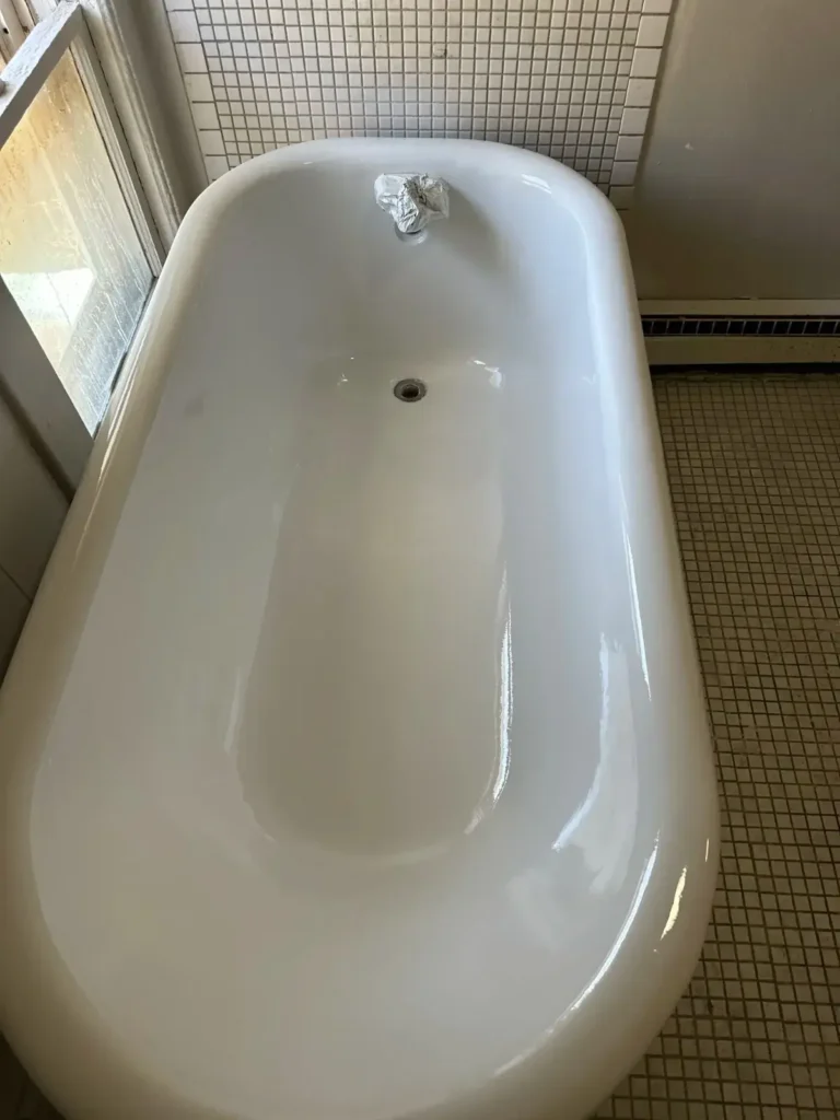 Close-up view of a white bathtub and surrounding white tiled walls, which appear to have been recently refinished. There is a black towel bar on the left wall and a black soap dish holder inside the tub area.